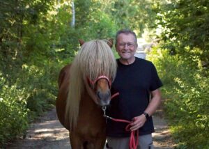 Peter Menzel führ einen Isländer am Führstrick über einen sonnigen Waldweg